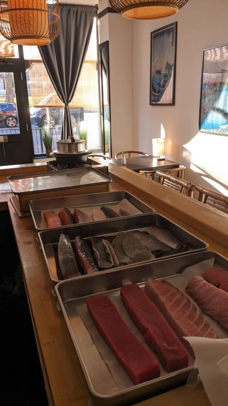 Trays of tuna, salmon and silver fish along the counter in afternoon light.